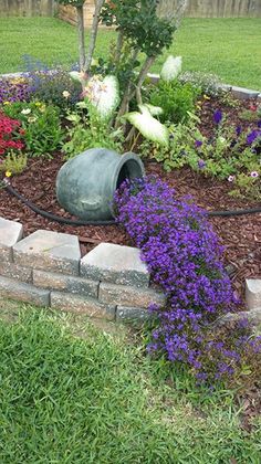 a garden with purple flowers in the middle and green grass on the ground next to it