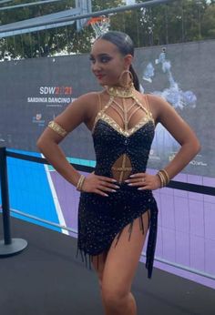 a woman in a black and gold dress posing for the camera with her hands on her hips