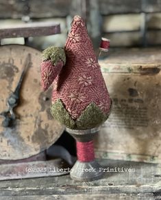 a red and green stuffed animal sitting on top of a wooden table next to some spools of thread