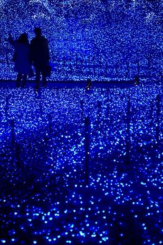 two people standing next to each other in a field with blue lights on the ground