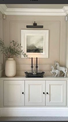 a white cabinet with two candles on top and a painting in the corner above it