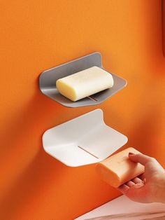 a person holding a piece of cheese in front of a wall mounted soap dispenser