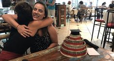 two women hugging each other in front of a cake on a table at a restaurant