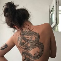 a woman with a dragon tattoo on her back is looking at the camera and has her hands behind her back