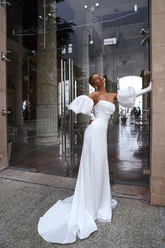 a woman standing in front of a glass door wearing a white dress with ruffle sleeves