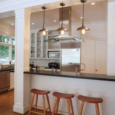 three stools in front of a kitchen island with lights hanging from it's ceiling