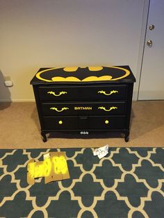 the batman dresser is painted black with yellow paint and has an open bat symbol on it