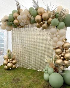 an arch made out of balloons and greenery in front of a white canvas backdrop