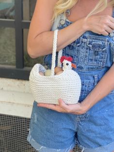 a woman wearing overalls and holding a white bag with a chicken on the front