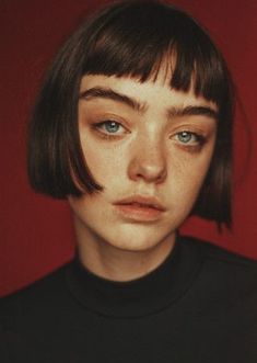 a woman with short hair and blue eyes wearing a black t - shirt against a red background