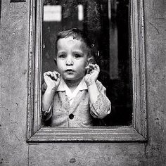 a young boy standing in front of a window with his hands on his head and looking at the camera