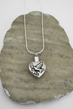 This dove memorial capsule necklace is shaped like a heart. It makes a great urn necklace for those who have lost a loved one or beloved pet. This necklace unscrews at the top to review the shallow hollow interior. Very sturdy. We recommend choosing the rope, curb or snake chain for the weight of the pendant. THIS NECKLACE INCLUDES: - stainless steel hollow heart urn pendant (30 mm | 1 1/5 inch) - a sterling silver rope, curb, snake or anchor chain (14 to 36 inches) *Add personalized charms by f Engraved Heart Charm Necklaces For Memorial, Silver Heart Pendant Necklace For Remembrance, Memorial Heart Charm Necklace, Engraved Heart Charm Necklace For Memorials, Memorial Heart Charm Open Heart Necklace, Memorial Open Heart Necklace With Heart Charm, Memorial Open Heart Charm Necklace, Memorial Open Heart Necklace, Memorial Silver Heart Charm Necklace