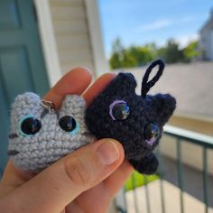 two small crocheted animals are being held by someone's hand in front of a house