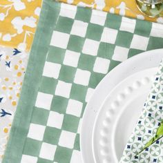 a green and white place setting with napkins, flowers and wine glasses on the table