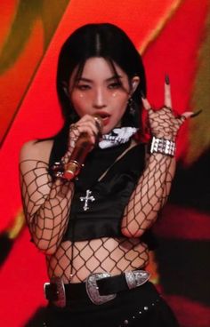 a woman in fishnet clothing holding a microphone up to her face and making the peace sign