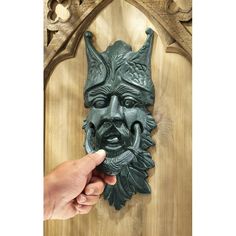 a hand holding a green mask on top of a wooden door with carvings around it