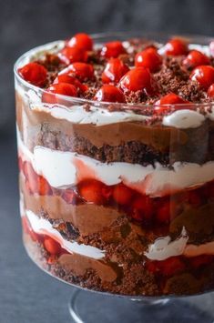 a layered chocolate cake with cherries and whipped cream in a glass dish on a black table