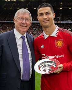 two men standing next to each other in front of a crowd holding a soccer trophy