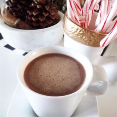 there is a cup of hot chocolate next to some candy canes and pine cones