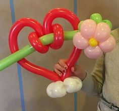 a woman holding two heart shaped balloons and a flower on top of it, in front of a blue striped wall