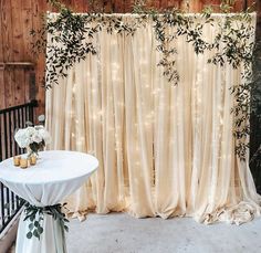 a white table topped with a vase filled with flowers next to a window covered in curtains