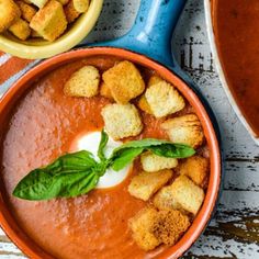 two bowls filled with soup and croutons on top of a table