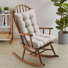 a rocking chair with a cushion on it in a living room next to a potted plant