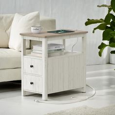 a white table with two drawers and a book on it in front of a couch