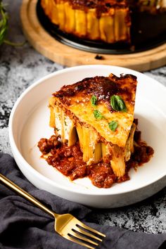 a white plate topped with lasagna covered in sauce and cheese next to a fork