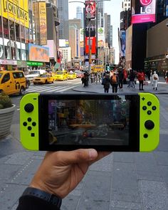 a person holding up a yellow nintendo wii game controller in the middle of a busy city street