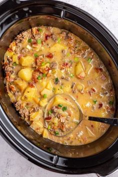 a crock pot filled with soup and potatoes on top of a table next to a spoon