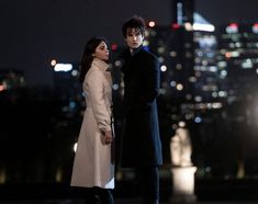 a man and woman standing next to each other in front of a city at night