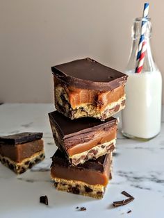 four pieces of chocolate chip cookie bars stacked on top of each other next to a glass of milk