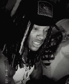 a black and white photo of a man with dreadlocks wearing a baseball cap