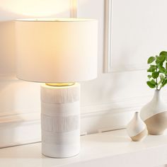 a white lamp sitting on top of a table next to a vase with a plant in it