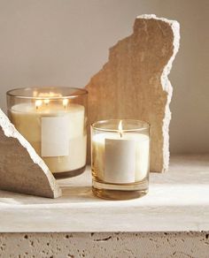 two candles sitting on top of a table next to a rock and paperweights