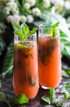 two glasses filled with drinks sitting on top of a table next to flowers and greenery