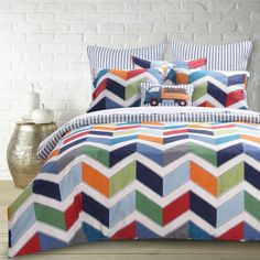 a bed with colorful comforters and pillows on it in front of a brick wall