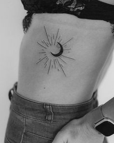 a black and white photo of a woman's stomach with a sun tattoo on it