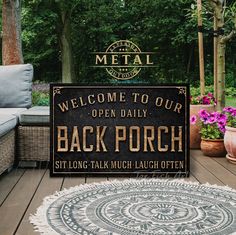 a welcome sign to the back porch with flowers and potted trees in the background