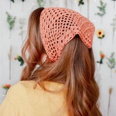 a woman with long red hair wearing a crocheted headband in front of flowers