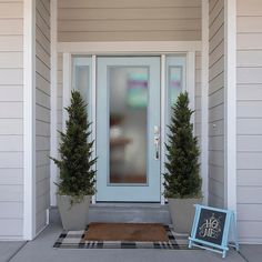 two potted trees on either side of the front door with a welcome sign in front