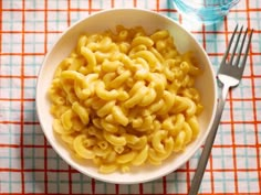 a white bowl filled with macaroni and cheese next to a fork on top of a table