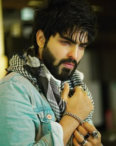 a man with a beard is wearing a scarf and looking at his watch on his wrist