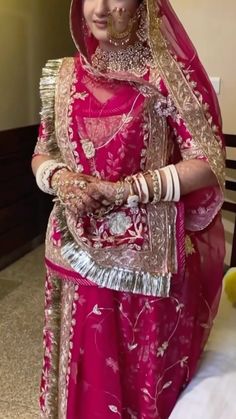 a woman in a red and gold bridal outfit standing next to a bed with her hands on her hips