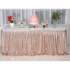 a table covered in pink sequins with a cake and flowers on it's side