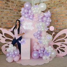 a woman standing in front of a pink and white balloon arch with butterflies on it