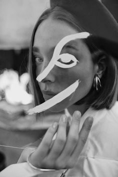 a woman with white paint on her face and hand in front of her face, looking at the camera