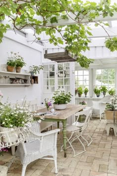 a table and chairs in a room with potted plants on the windowsills