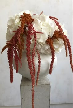 a white vase filled with lots of flowers on top of a cement block in front of a wall